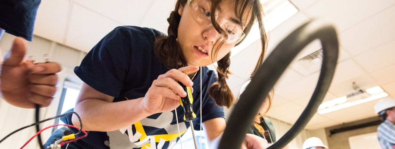 A student holds a screwdriver and she adjusts her project in the Collegiate Wind Competition