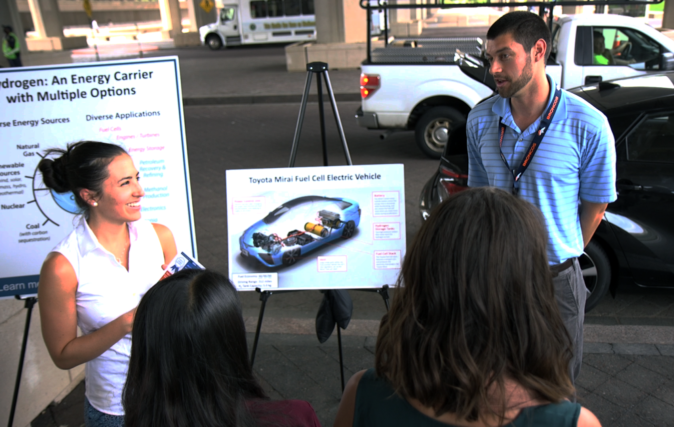 Two people stand in front of posters about fuel cell electric vehicles.