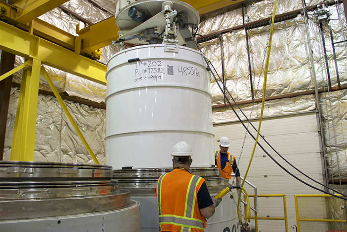 Operations technicians Larry Hampton and Gerardo Lazalde load a 4,855-pound transuranic waste package into a shipping container at the Idaho Site.