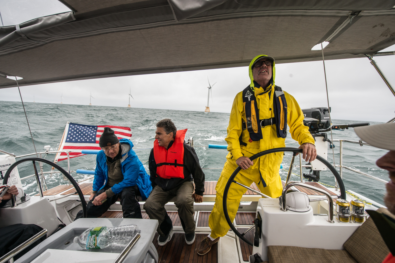 Three men aboard a boat with offshore wind turbines in the background