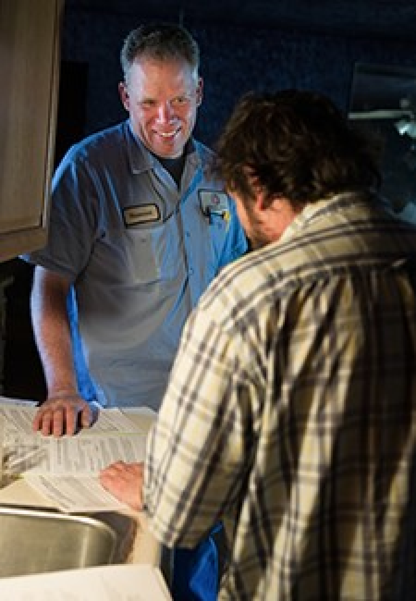 Photo of two men standing and talking. One of the men wears a workshirt with his namepatch on it.