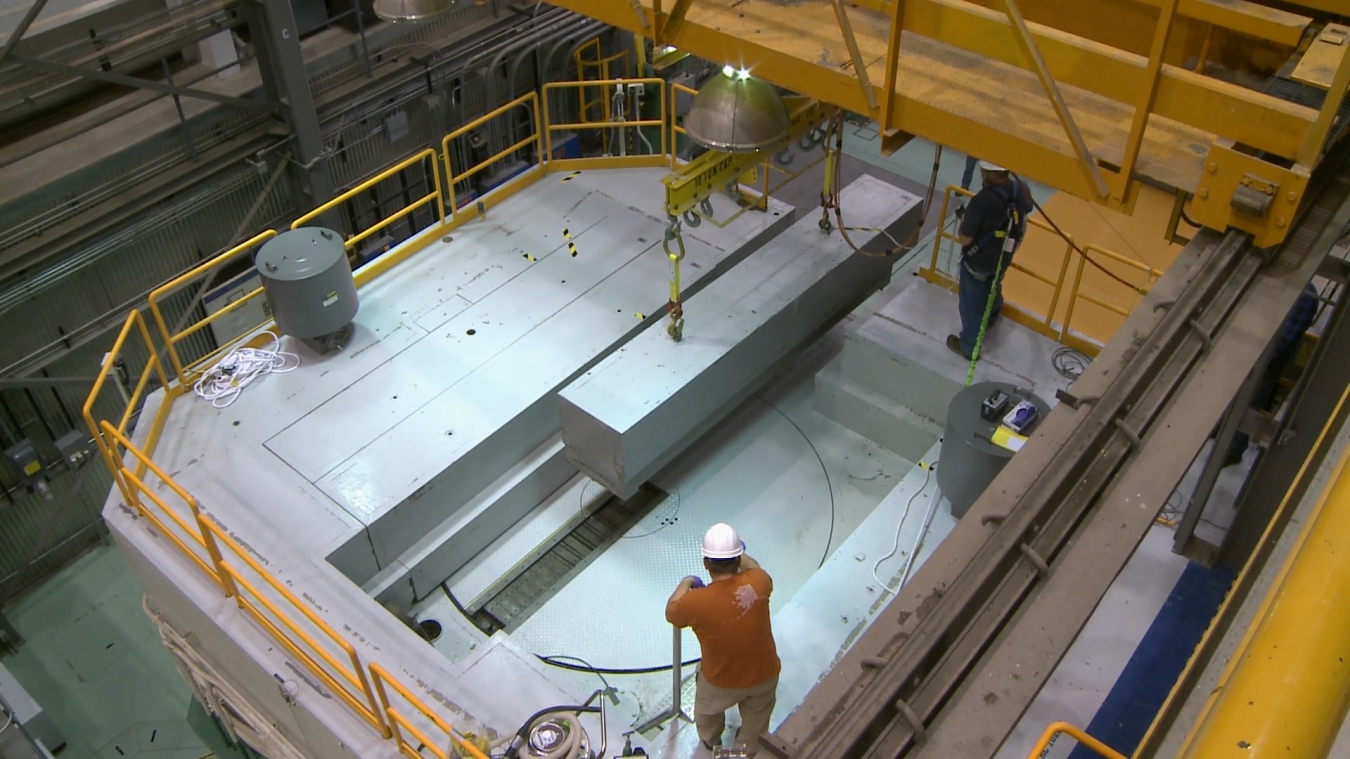 A worker looks on as a crane helps to remove a part of the nuclear reactor's shield block.