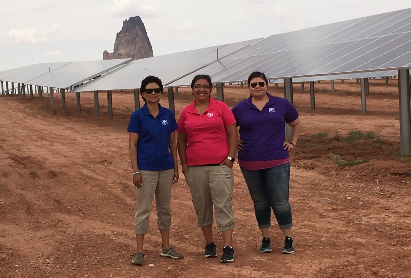 Three women standing in front of solar panels.