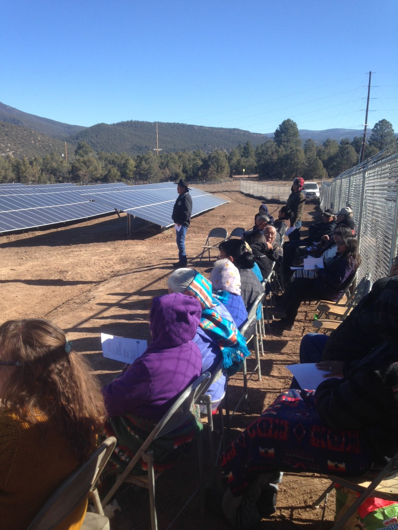 People sitting in chairs alongside fence and solar arrays.