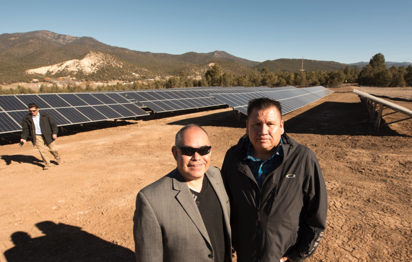 Two men stand in front of solar array.