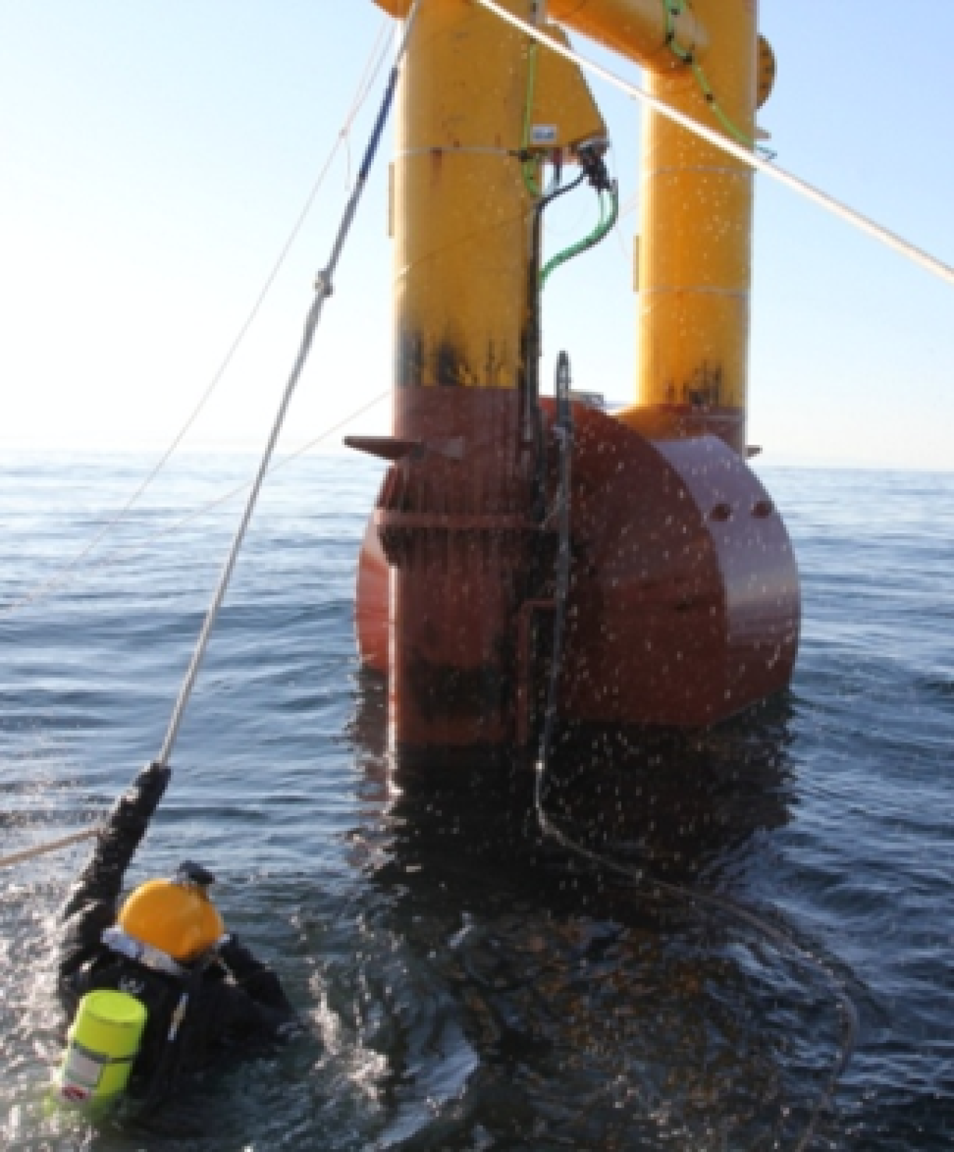 A man in scuba gear holding onto a wire from a point absorber in open water.