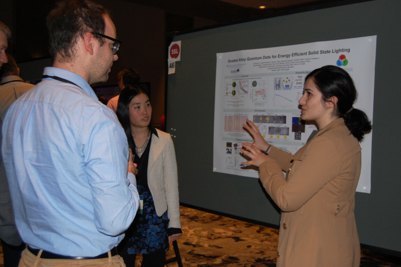 A photo from the 2018 SSL R&D Workshop showing three people discussing a technical poster. 