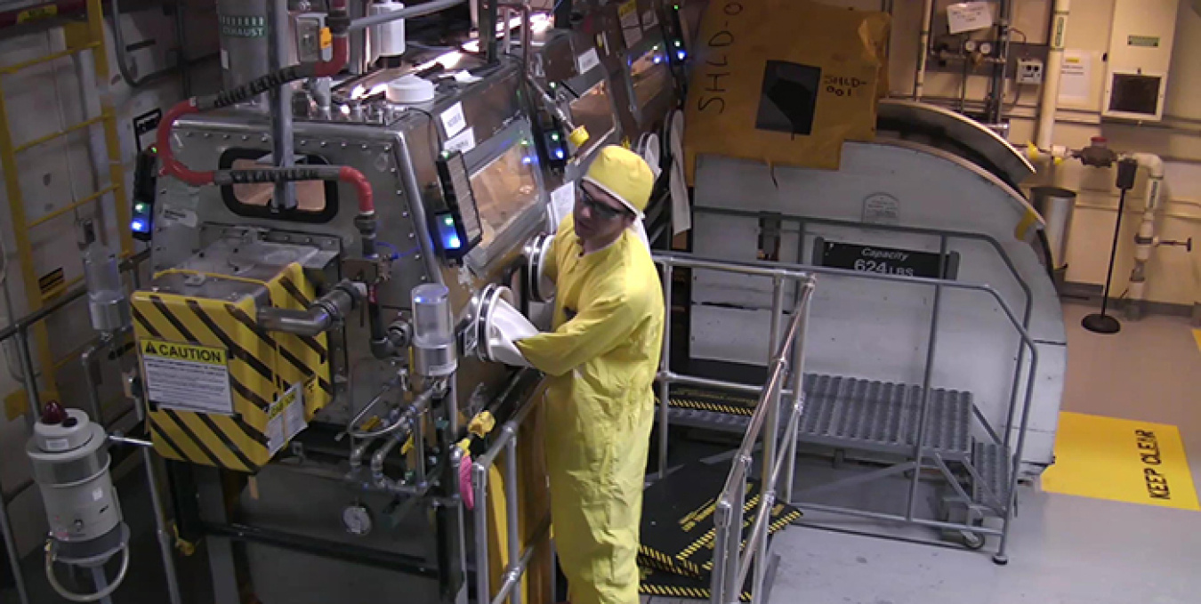 A worker manipulates a glove box used to treat unremediated nitrate salt waste.