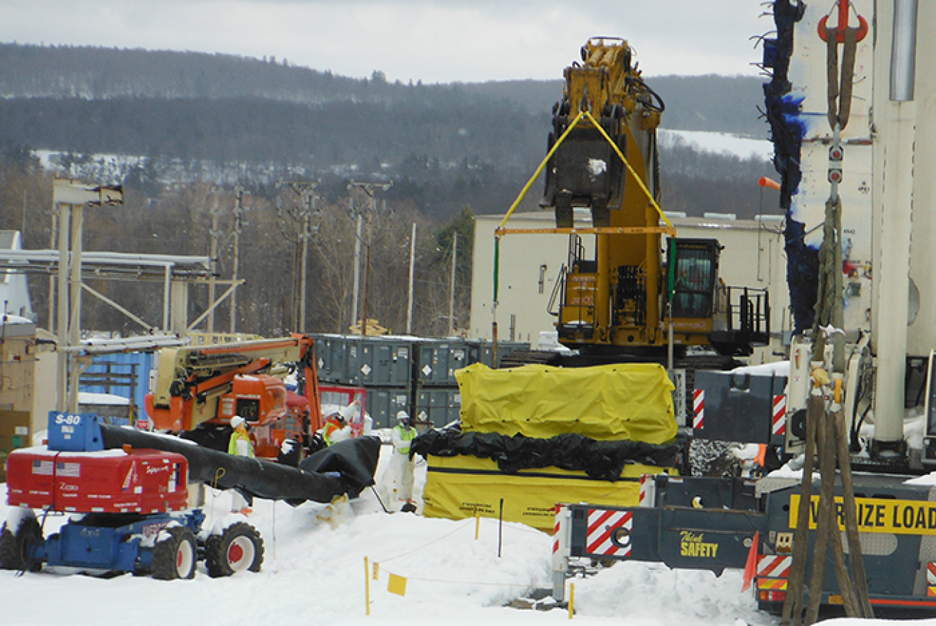 The second of four in-cell Vitrification Facility coolers, covered in yellow herculite, is lowered into a waste storage box. The waste box includes contamination controls and cribbing for safe transport and storage. 