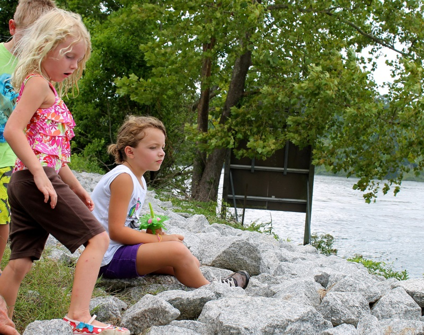 Photo of children sitting on rocks beside the water.