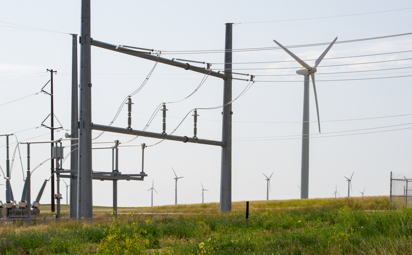 Electrical transmission lines in a field next to a wind turbine.