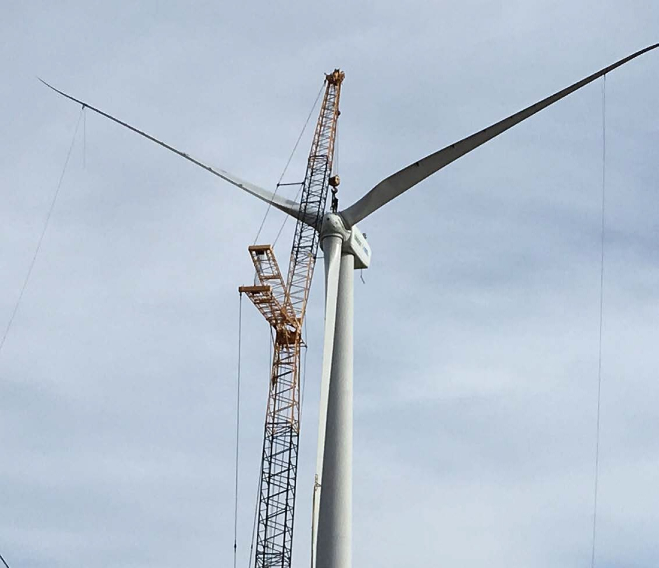 Photo of a wind turbine with crane propped up against it.