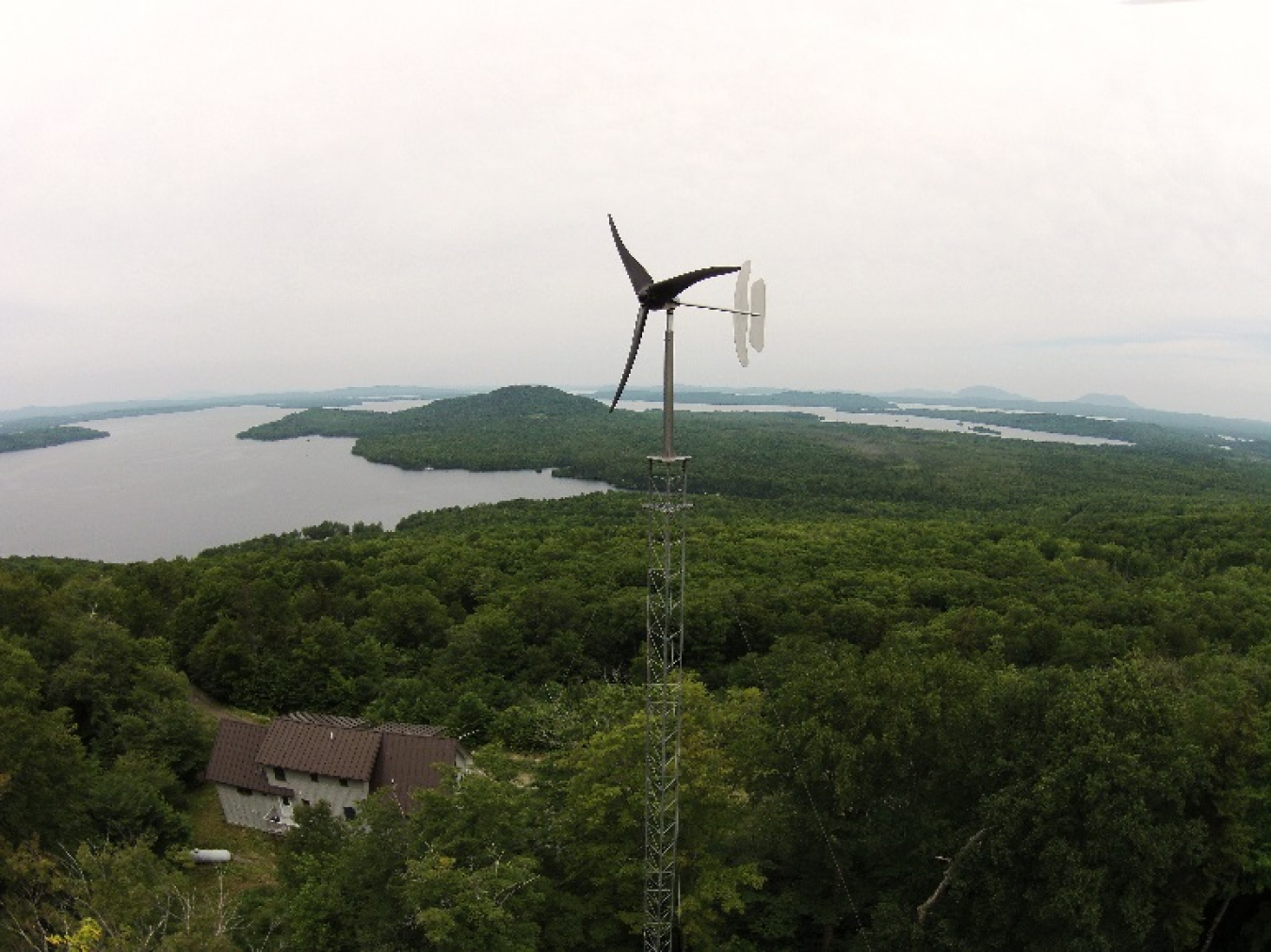 A small wind turbine in a wooded area by a lake.