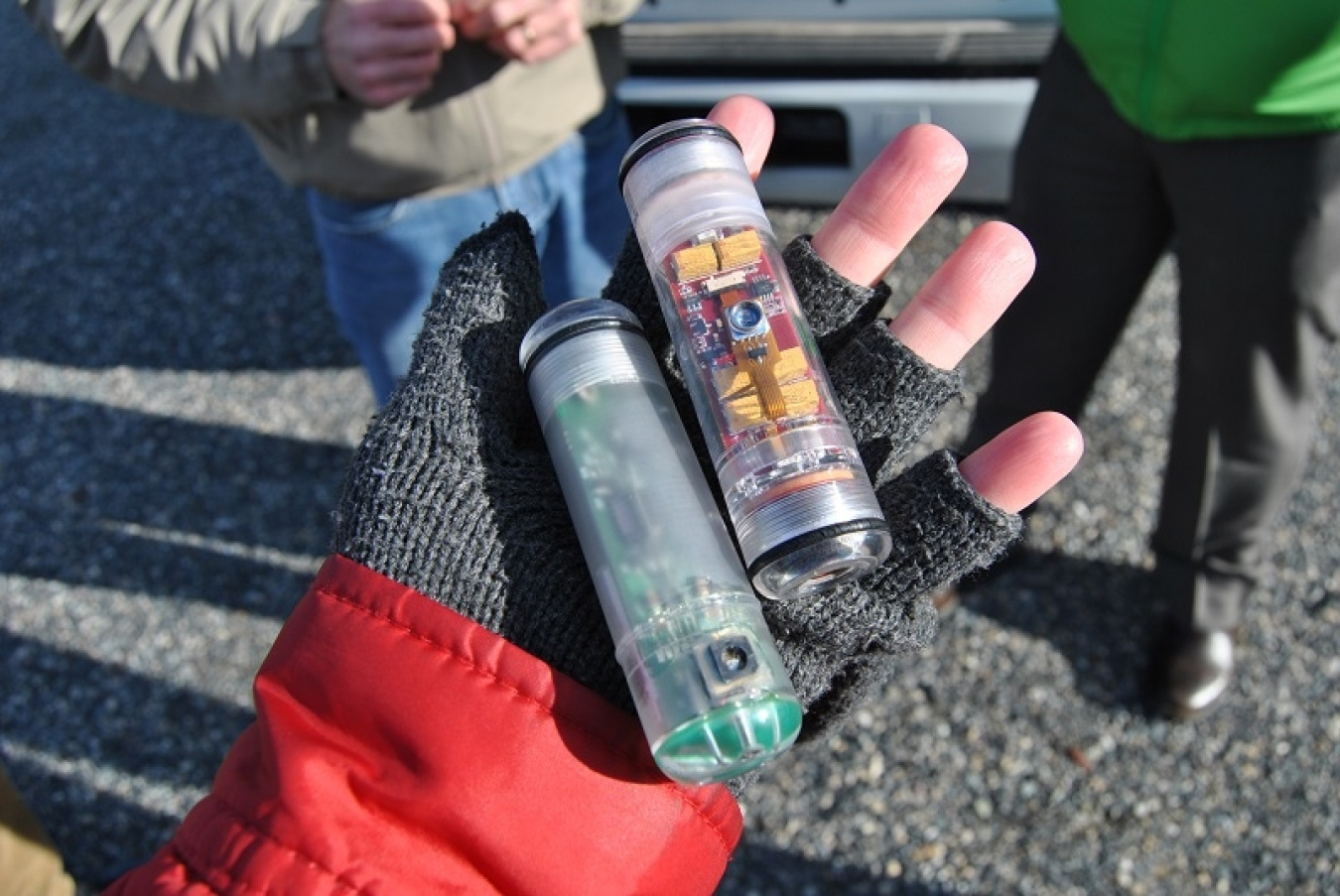 Closeup of a gloved hand holding two transparent plastic tubes full of sensors.