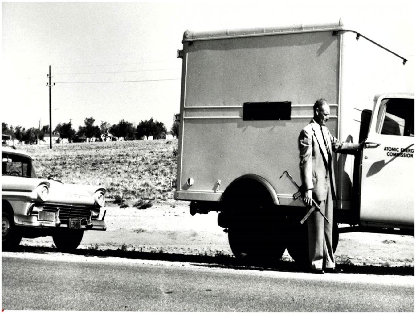 An Atomic Energy Commission courier in the late 1950s armed with an M3 submachine gun at the cab of a bobtail truck that carried high explosives. Behind the truck is a Ford ranch wagon used as an escort vehicle.