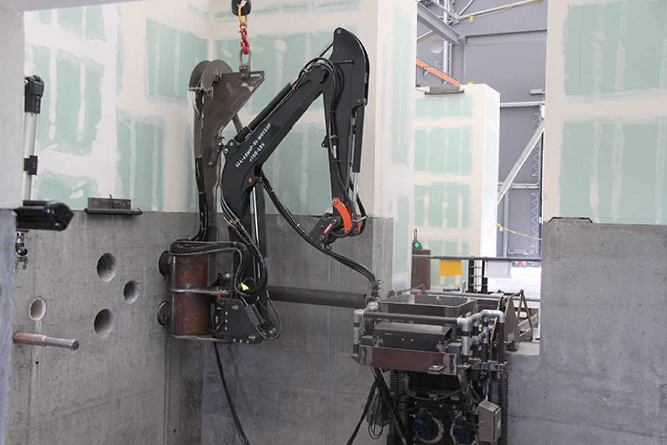 Crews attached a remote excavator to the wall at the 324 Building mockup. Installing the equipment required the precise drilling of support holes.