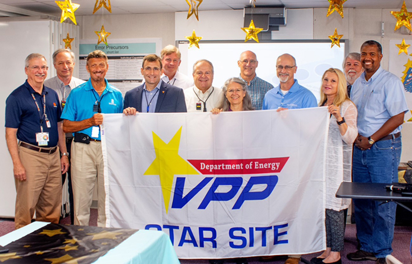 Employees from the Oak Ridge Office of Environmental Management and North Wind Solutions hold a flag that will hang at the Transuranic Waste Processing Center.