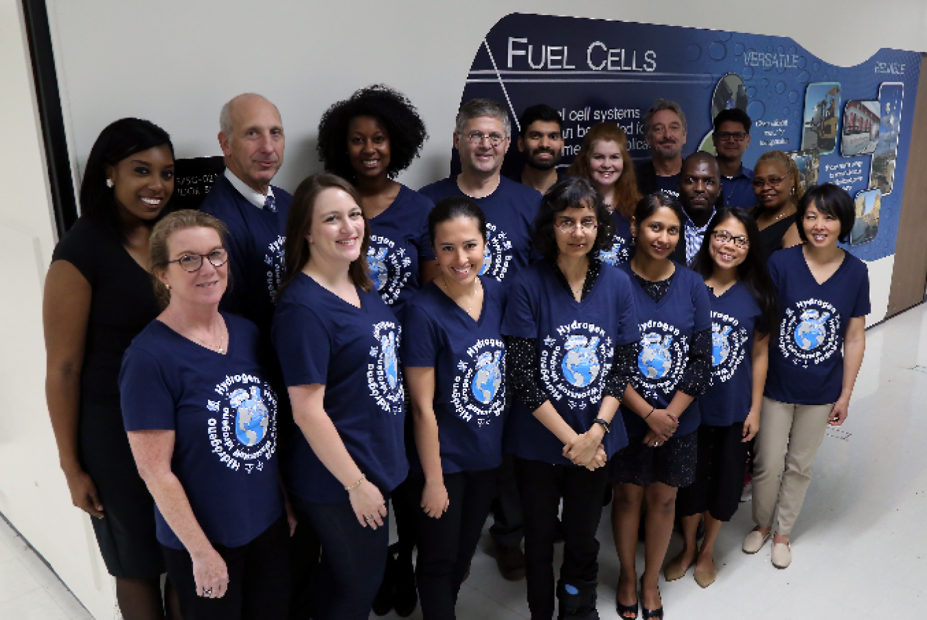 Photo of numerous people standing in front of a fuel cells sign.