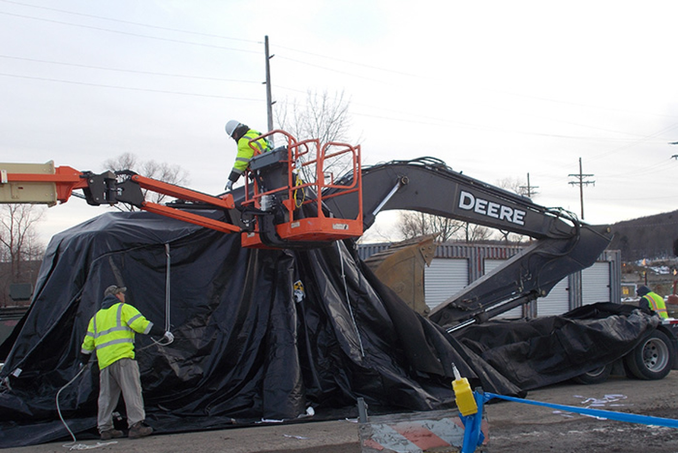 EM crews use a high lift to help remove a large cover off an excavator.