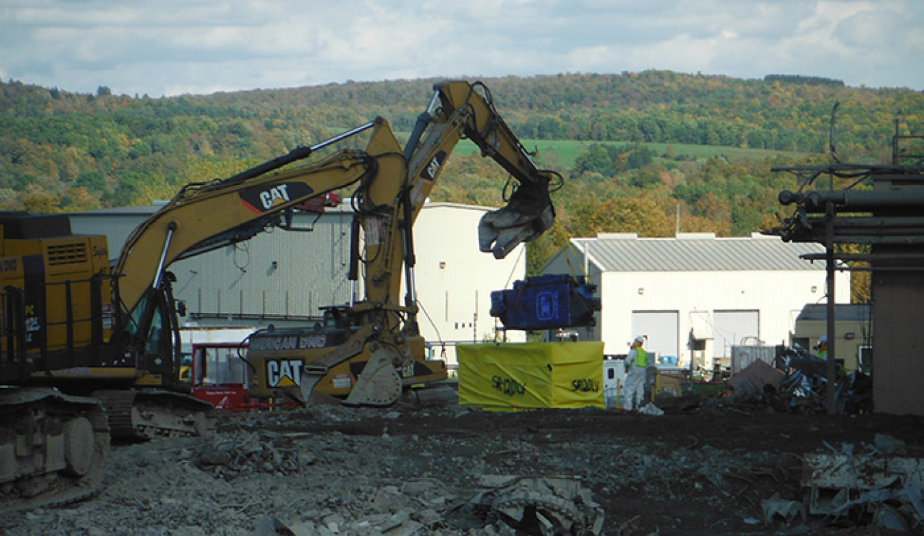 An excavator relocates a dust collector removed from one of two ancillary facilities workers recently demolished at the West Valley Demonstration Project.