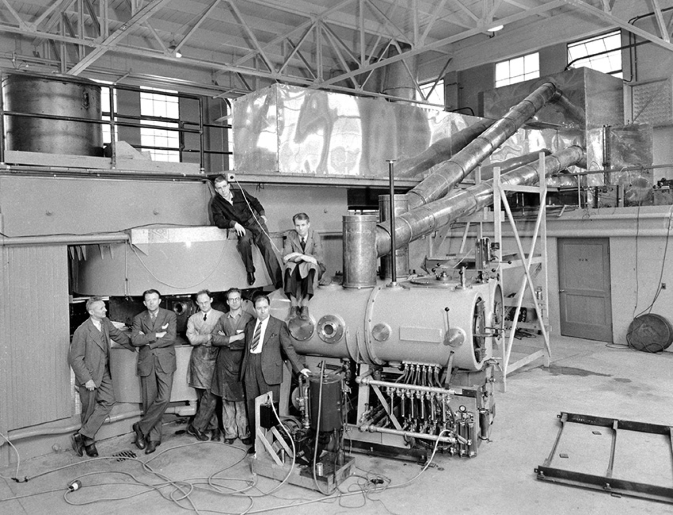 Posing with the newly completed 60-inch cyclotron in the Crocker Laboratory are (left to right) Donald Cooksey, Ernest O. Lawrence, R. Thornton, W. Salisbury and J. Backus and (on top) L. Alvarez and E. McMillan.