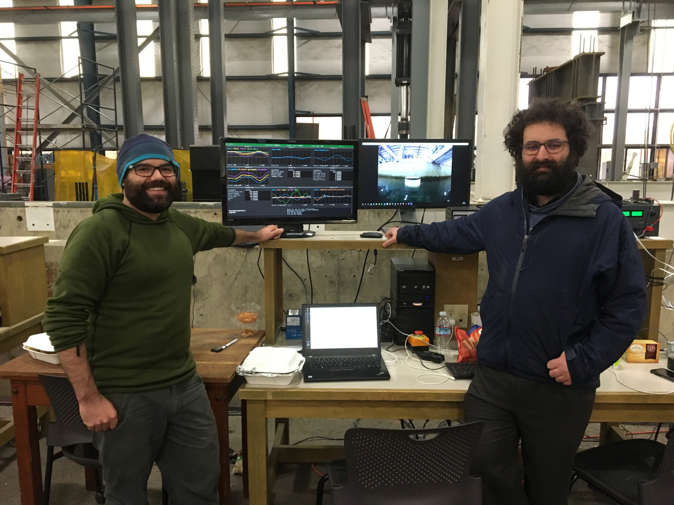 Aquaharmonics co-founders stand in front of a computer while their wave energy converter is being tested in a flume.