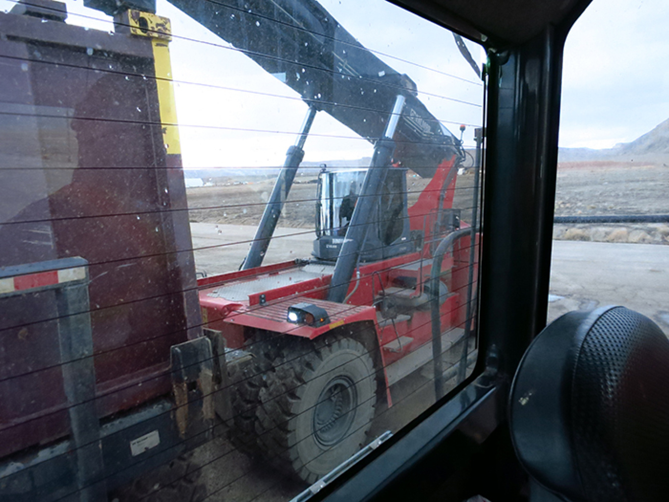 A reach stacker places a container of mill tailings from the train onto a haul truck for disposal at the Crescent Junction disposal cell, as seen from inside the truck’s cab.
