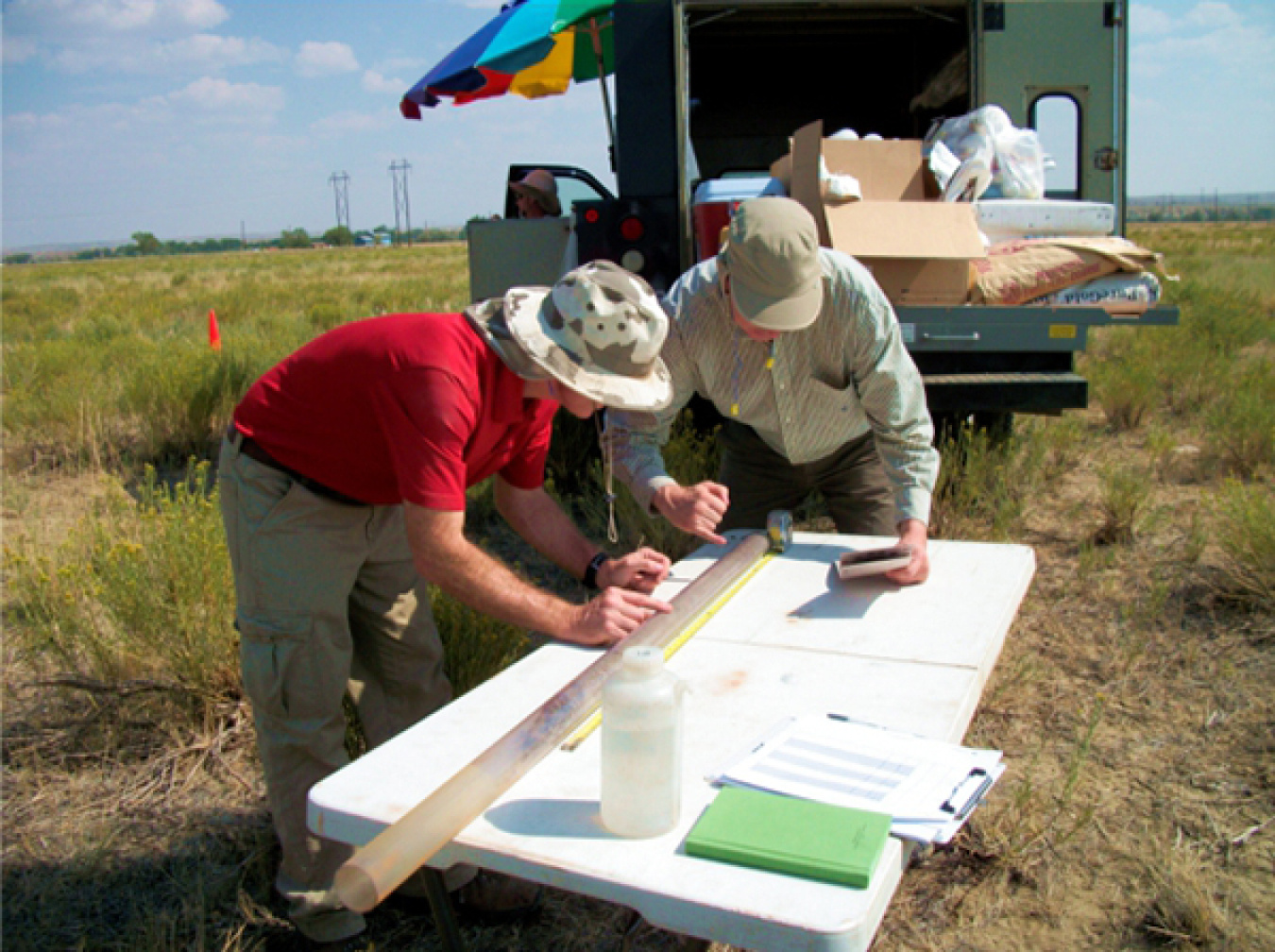 Bill Dam, on detail from U.S. Geological Survey, and an LM contractor employee examine a soil core collected inside a plastic tube.