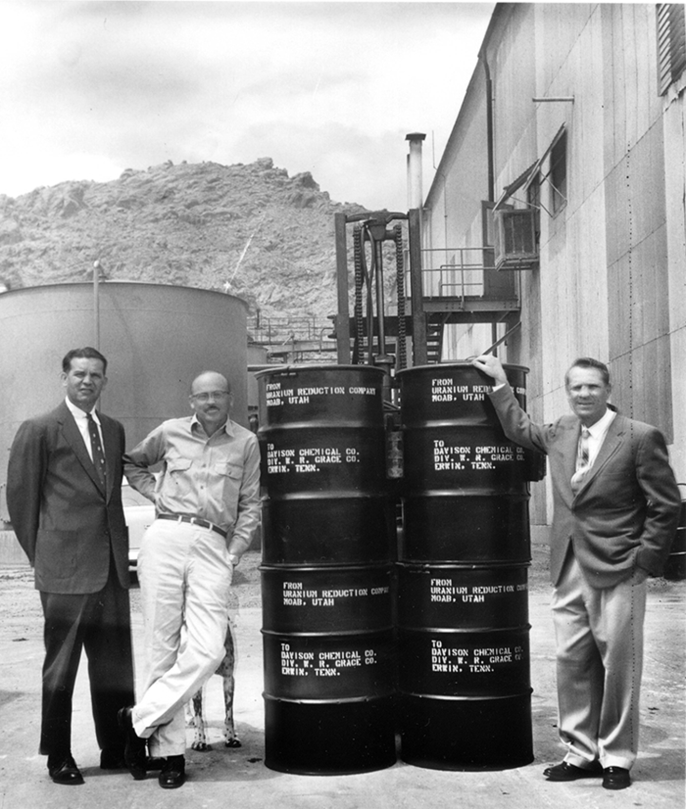 Charlie Steen, center, stands with his lawyer, Mitch Melich, and Uranium Reduction Company General Manager Ray Hollis, alongside barrels of yellowcake, or processed uranium ore. Steen’s dog, Butch, is in the background. Photo courtesy of the Moab Museum, 