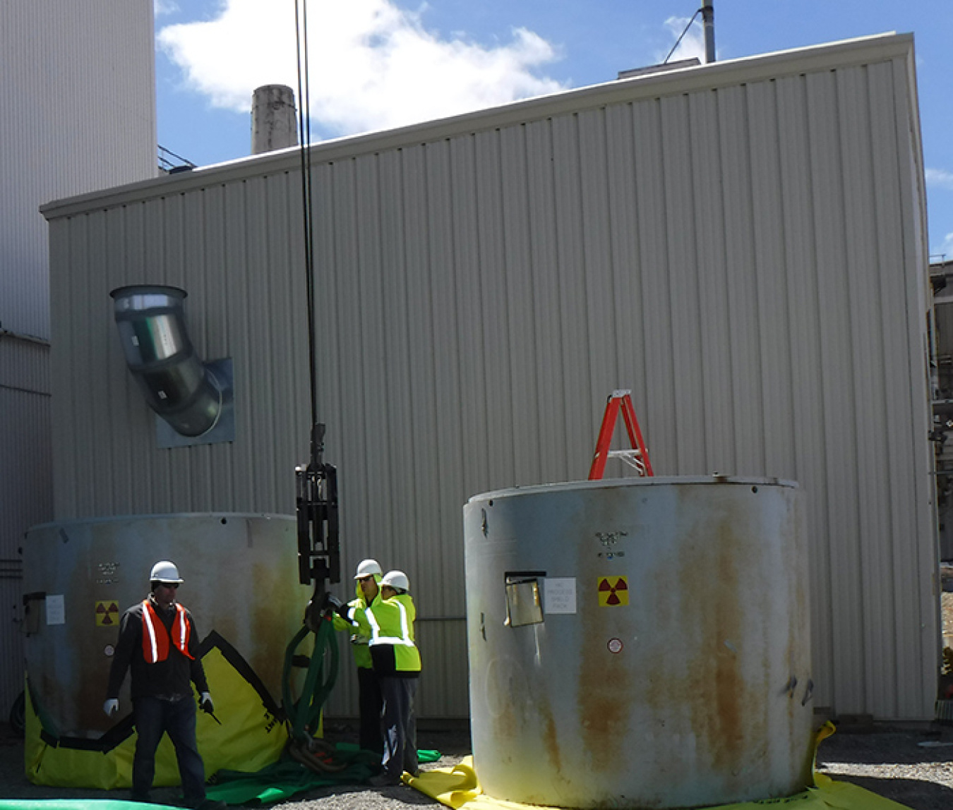 A crew safely finishes relocating two waste containers to their new location at an outdoor storage area.