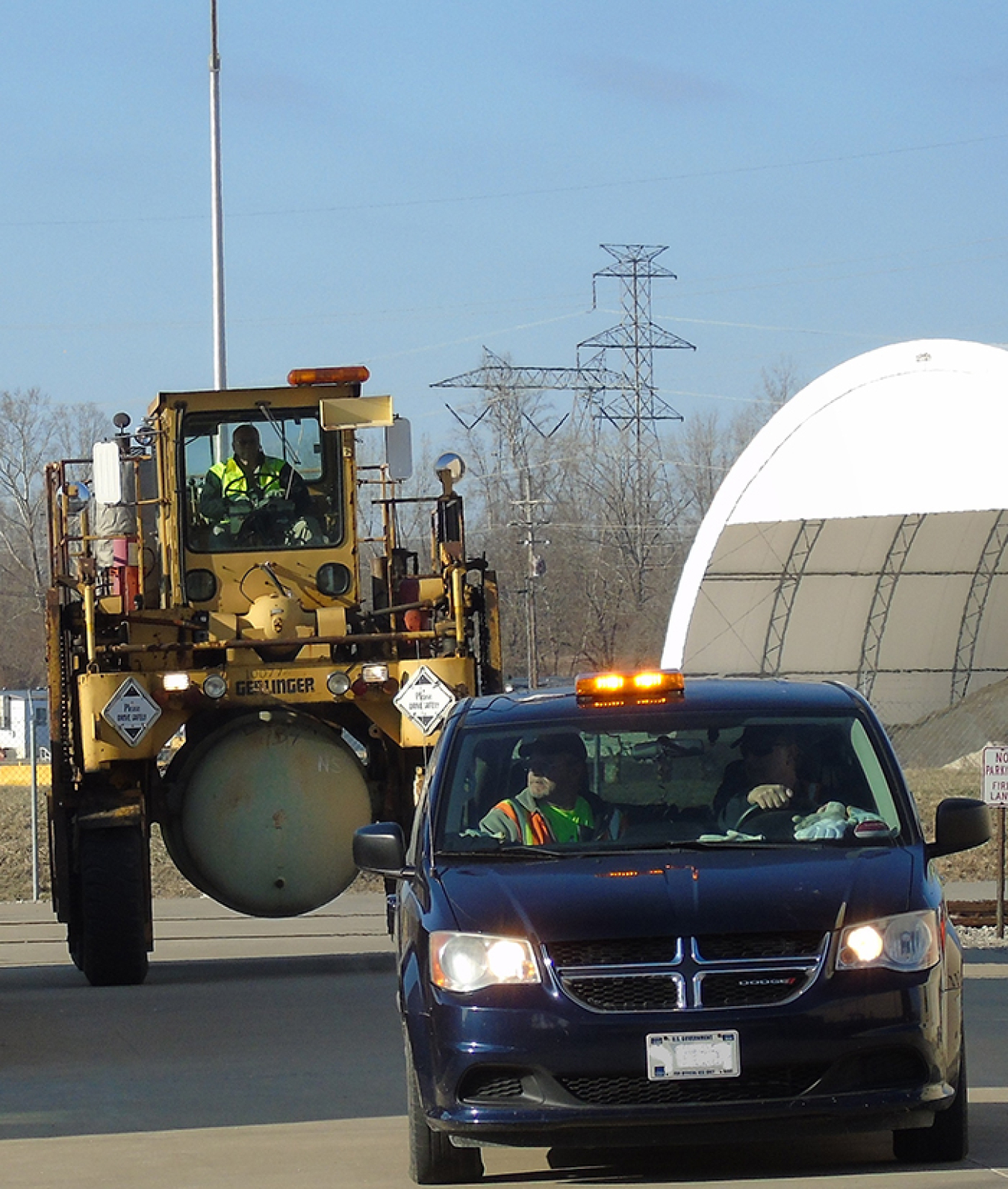 Mid-America Conversion Services’ Bill Bowen, right foreground, driving, and Phil Gullett escort straddle-carrier driver Ron Rinehart outside the Portsmouth Depleted Uranium Hexafluoride (DUF6) conversion facility.