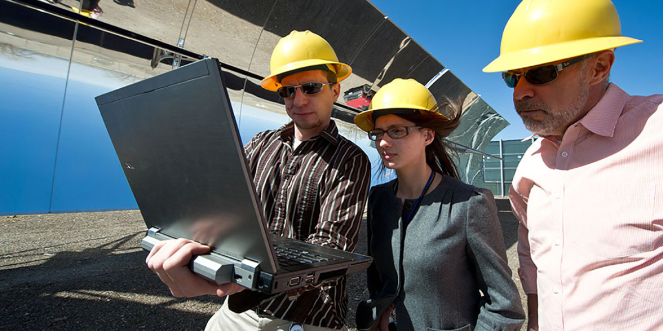 Three people looking at a laptop computer on a worksite.