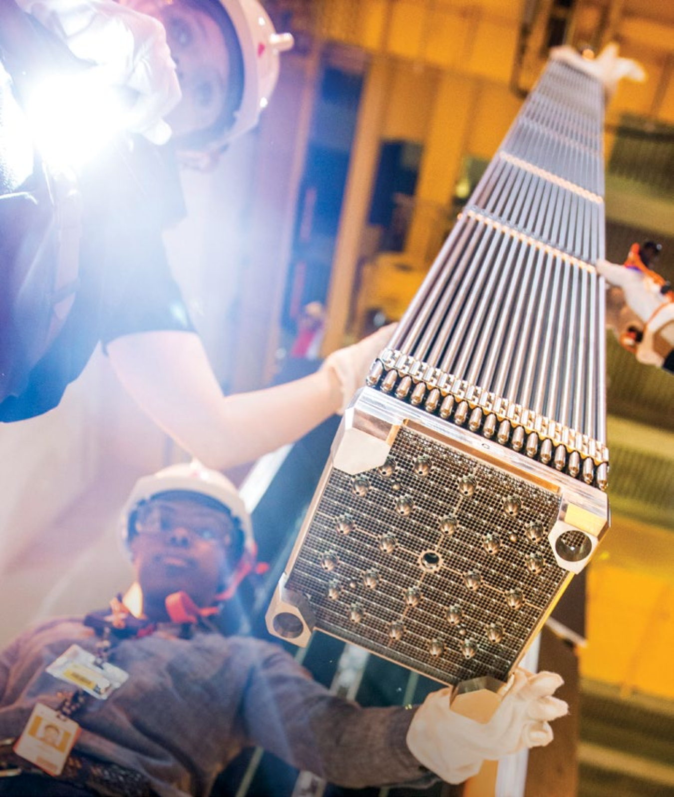 Workers inspect a nuclear fuel assembly being loaded into a nuclear reactor.
