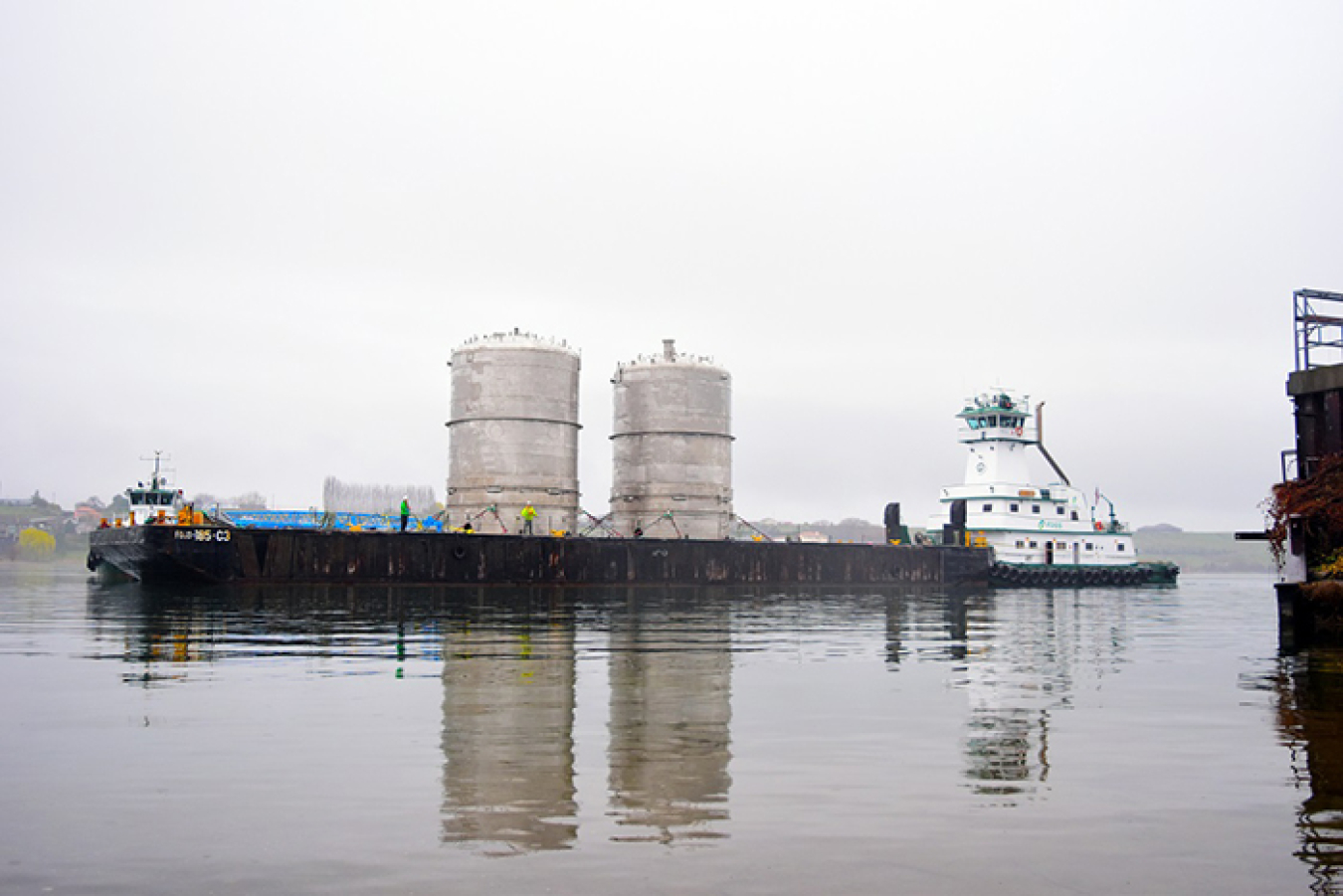 Two massive processing vessels, standing 40 feet tall and weighing 160 tons each, arrive by barge at the Columbia River Port of Benton to be offloaded by Lampson International.