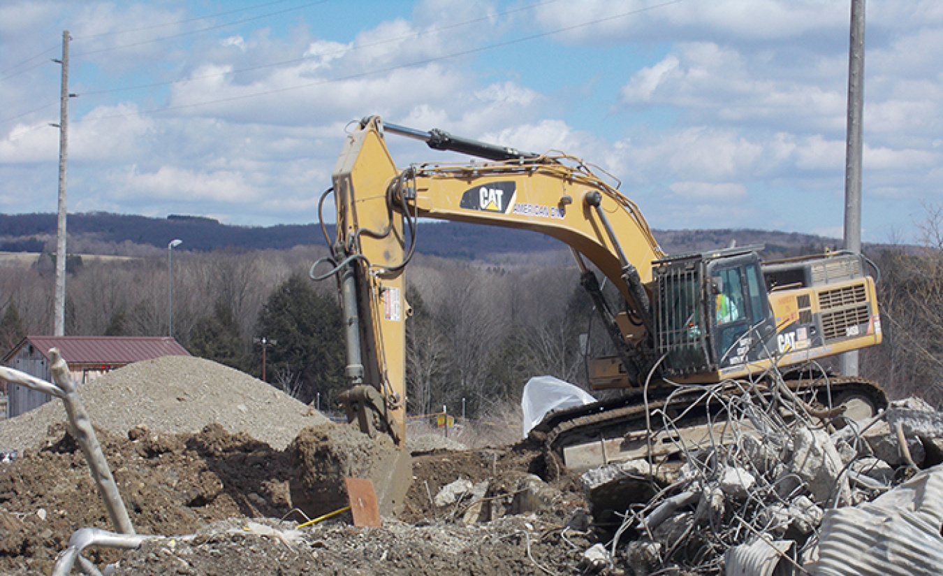 A large excavator digs near a sump that collected water from the drains of a facility formerly used to treat low-level waste.