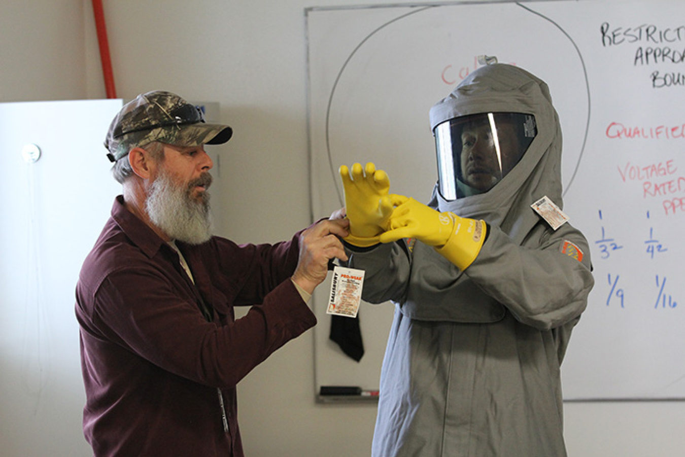 Trainer Gary Lyons, left, assists program manager Owen Peters in demonstrating the proper donning of arc flash personal protective equipment for a National Fire Protection Association class.