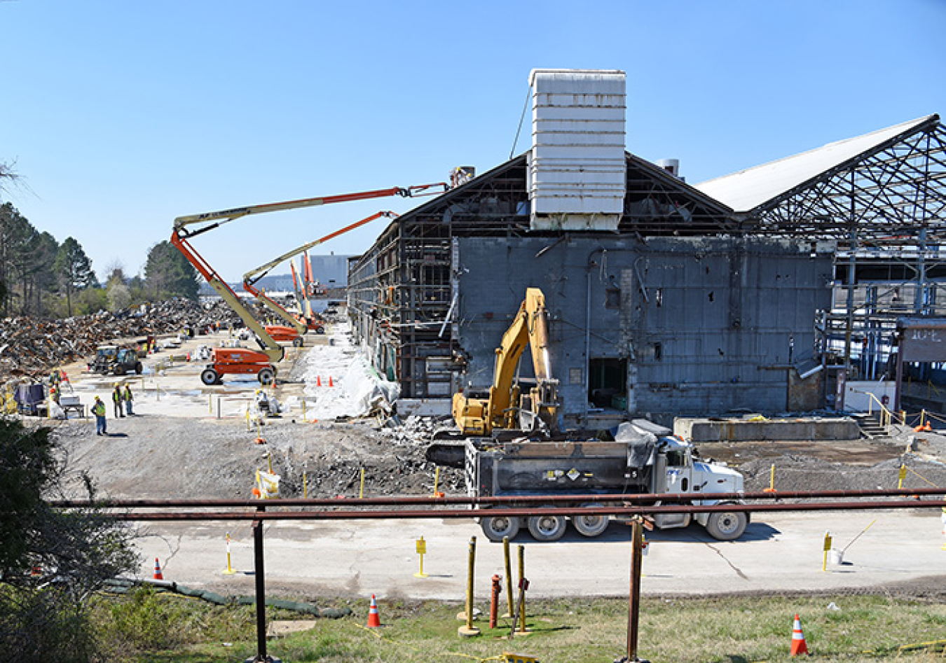 Oak Ridge Site workers remove asbestos-containing panels from portions of the K-1037 Building while demolition and debris removal are underway on other sections.