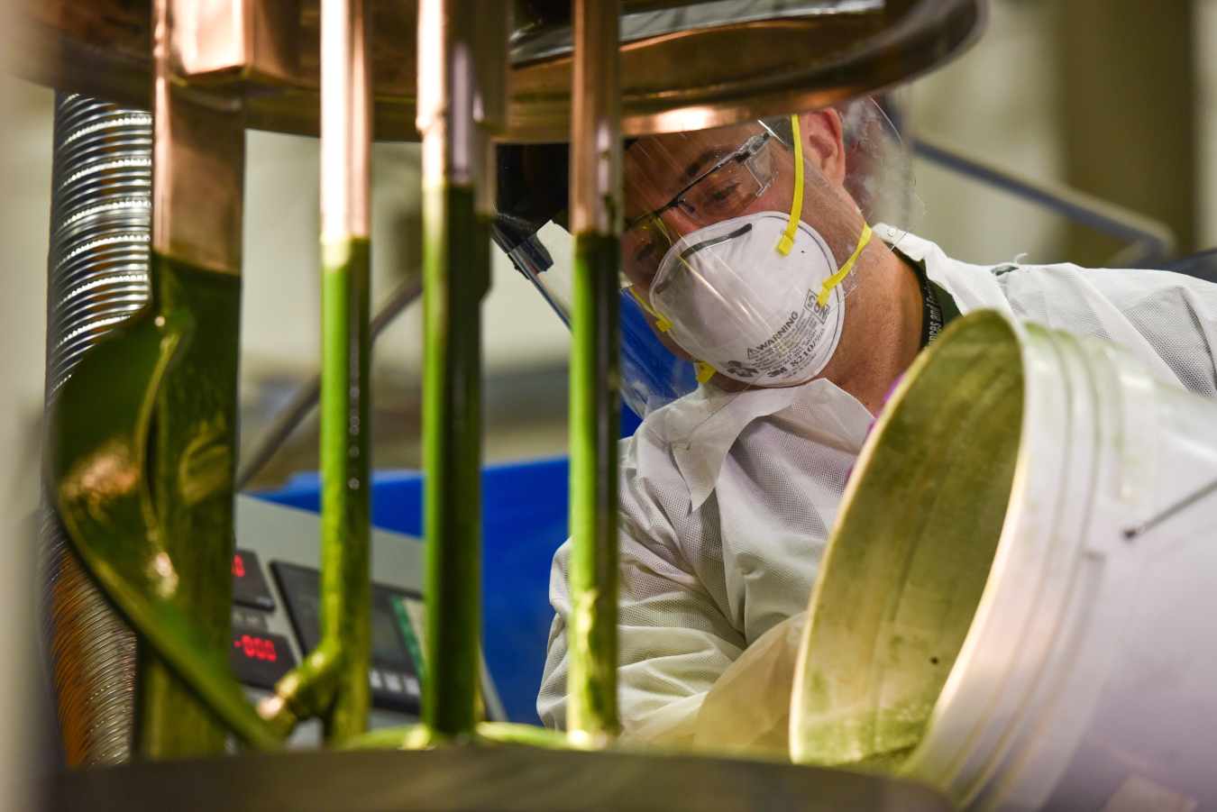 A lab tech working in a lab with a bucket of algae