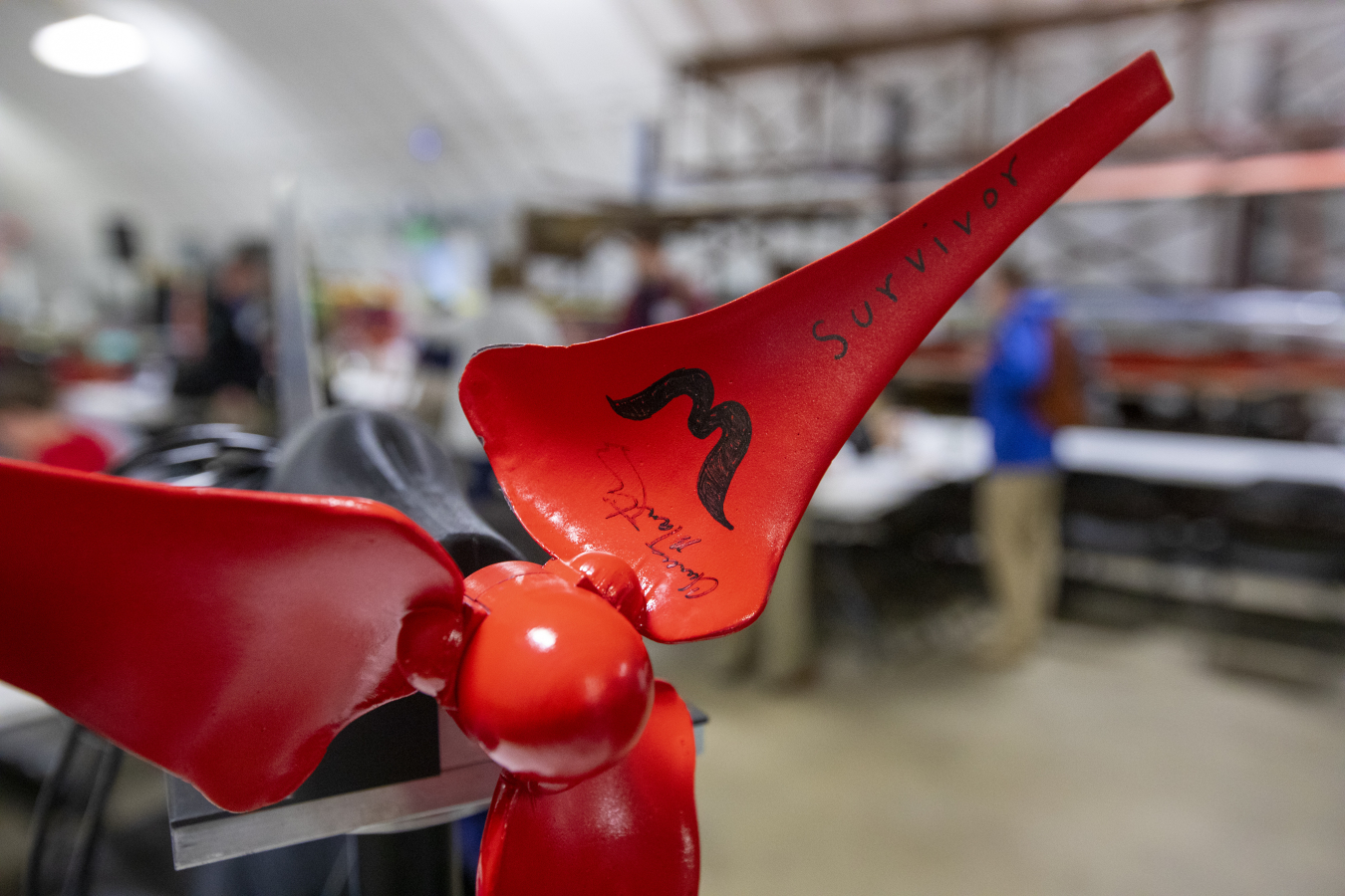 A model of a small-scale wind turbine with three red blades, including one that has the word, “Survivor” written on it in Sharpie.