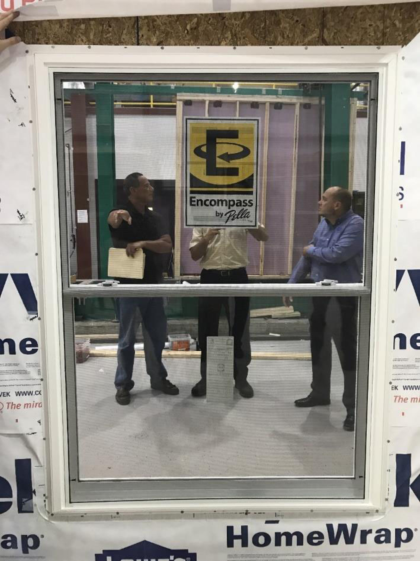 Three men standing behind an insulation window.