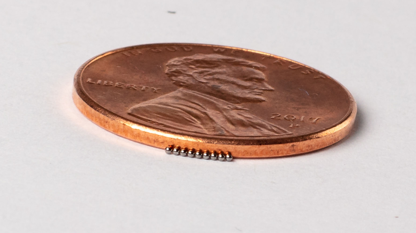 Closeup photo of a penny next to MiniFuel targets that look like tiny beads, to show scale.