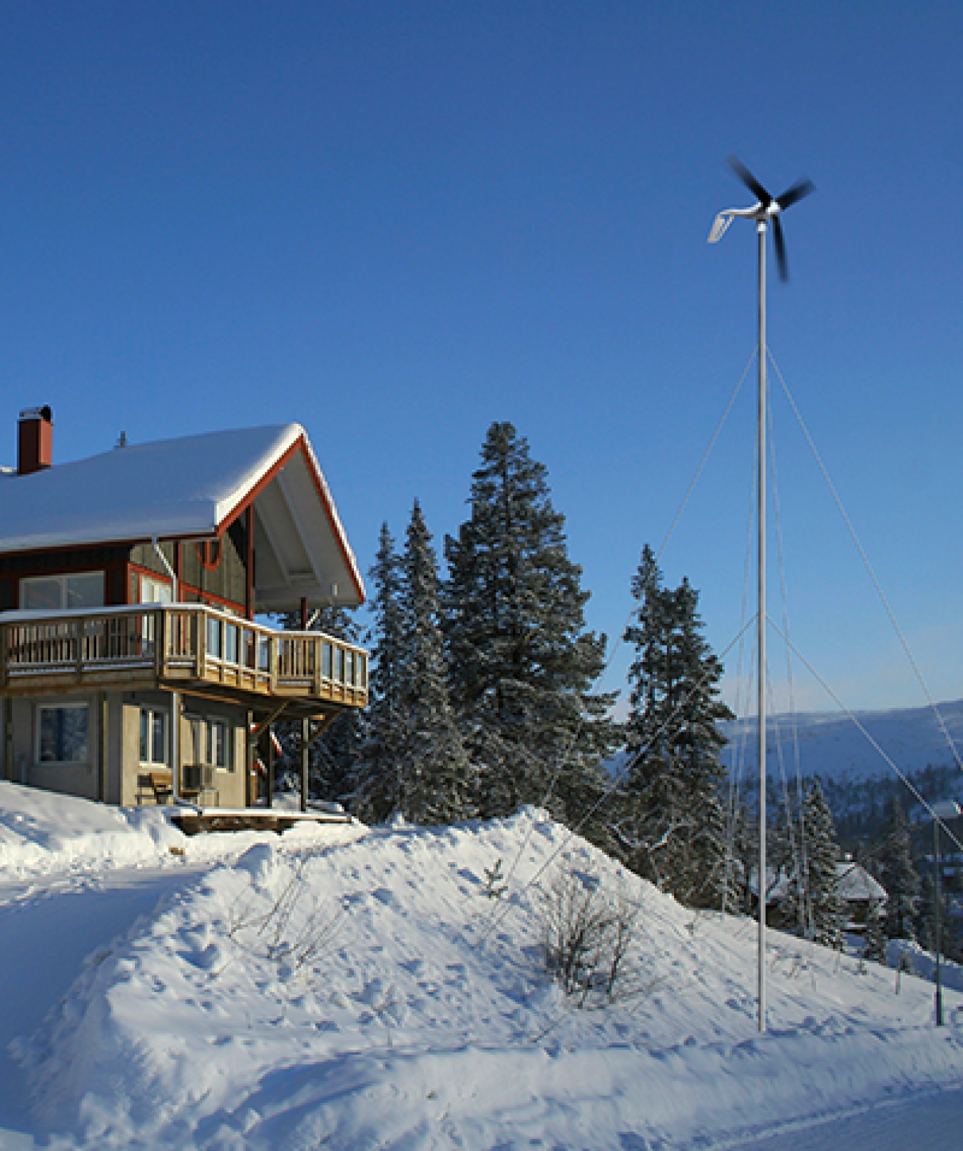 small wind turbine outside of a snowy cabin on a mountain.