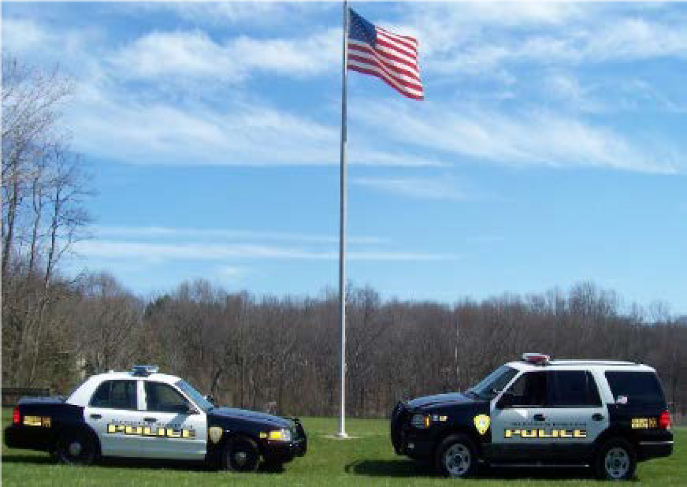 Photo of two police cars and an American flag behind.