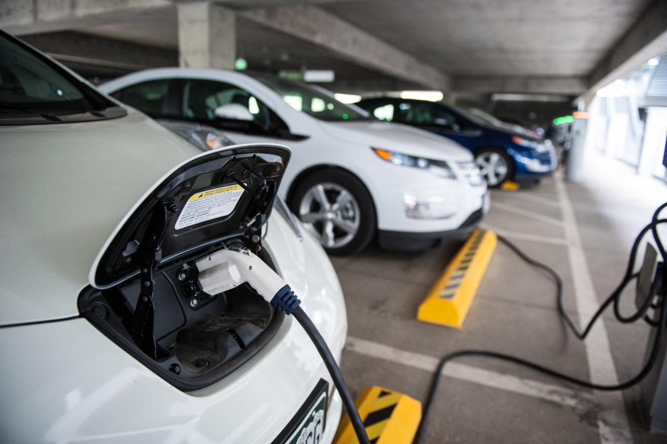 The front of an electric vehicle with a plug inserted into the battery at a charging station in the NREL garage.