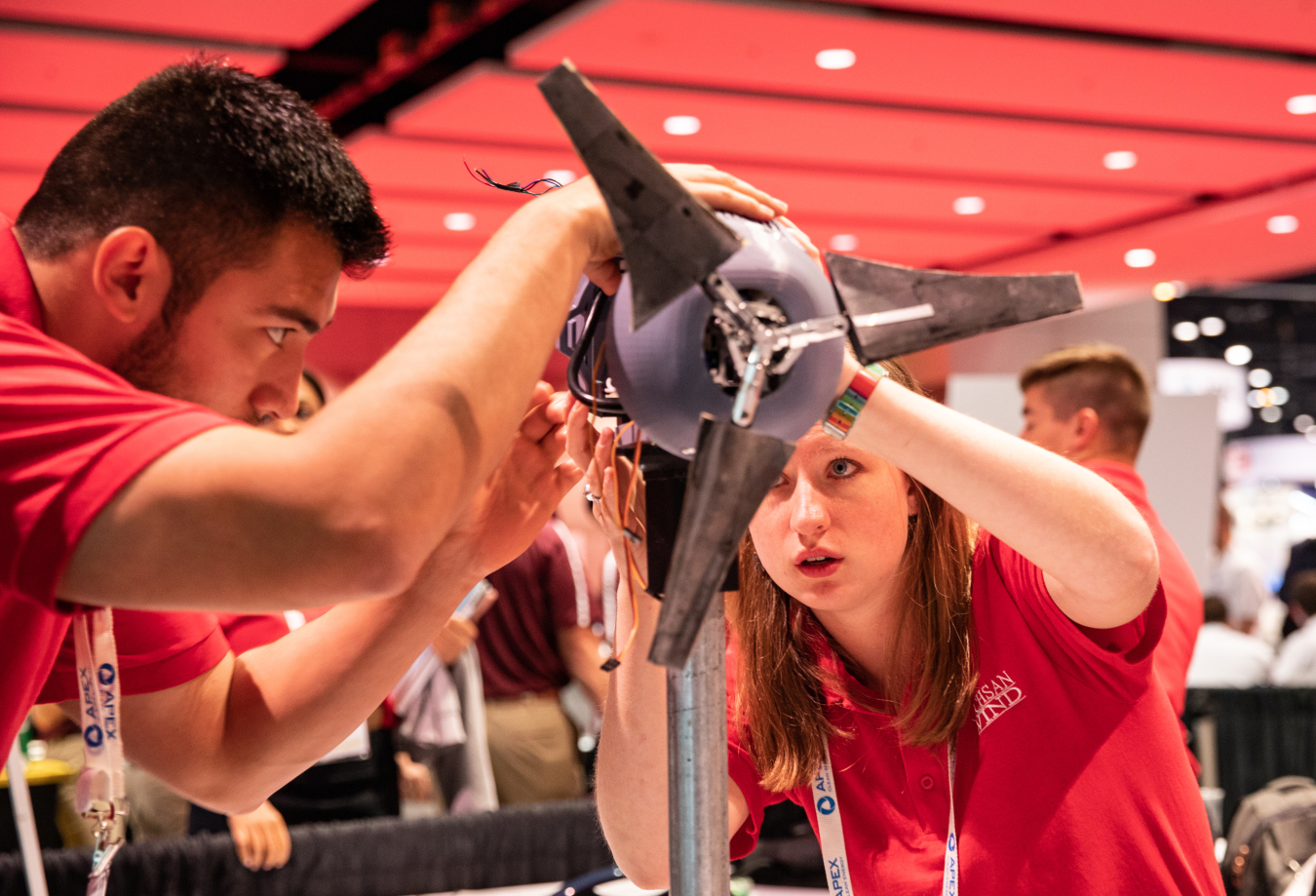 Two students wearing school shirts adjust the nacelle on a model wind turbine.