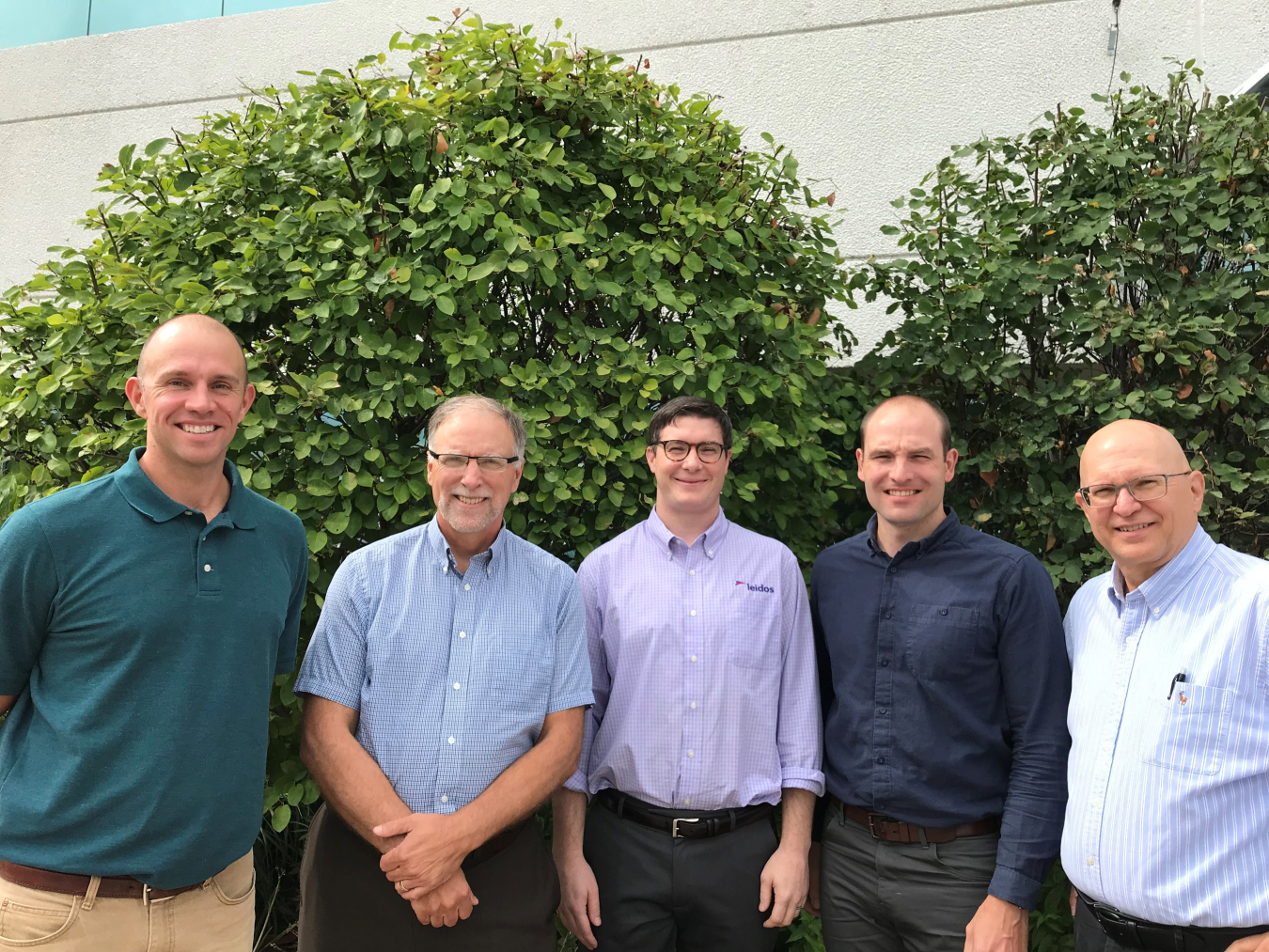 5 men standing in front of some bushes.