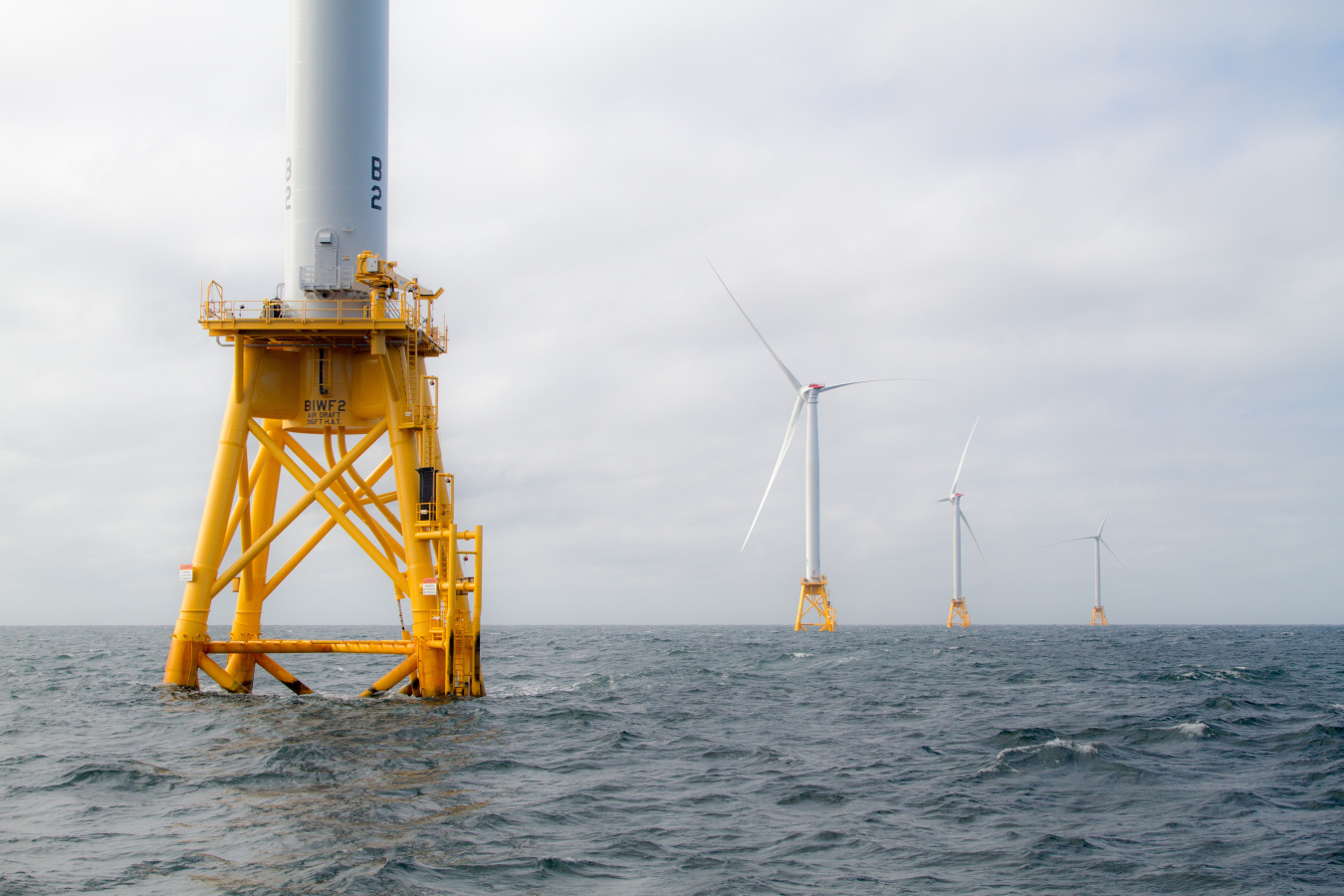 Photo of 4 wind turbines on orange platforms in the middle of ocean.