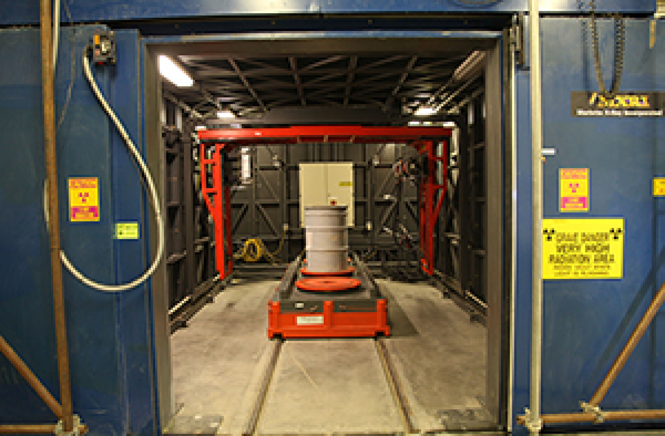 A view of the real-time radiography vault before the doors close and a waste container undergoes inspection by specialists in the adjacent control room.