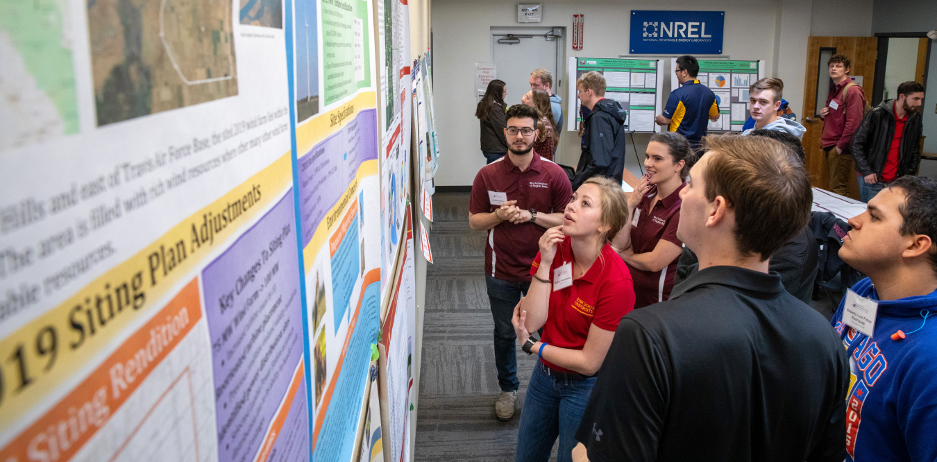 Students wearing shirts from different universities look at posters at the 2019 Collegiate Wind Competition.