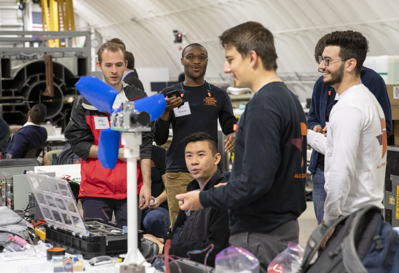 A group of students smile at a model wind turbine at the 2019 Collegiate Wind Competition.